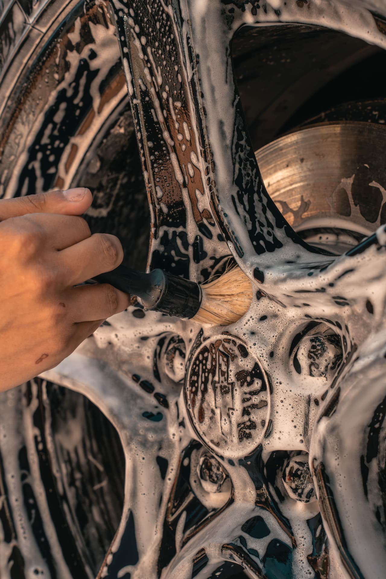 Detail brush working foam into a soapy alloy wheel
