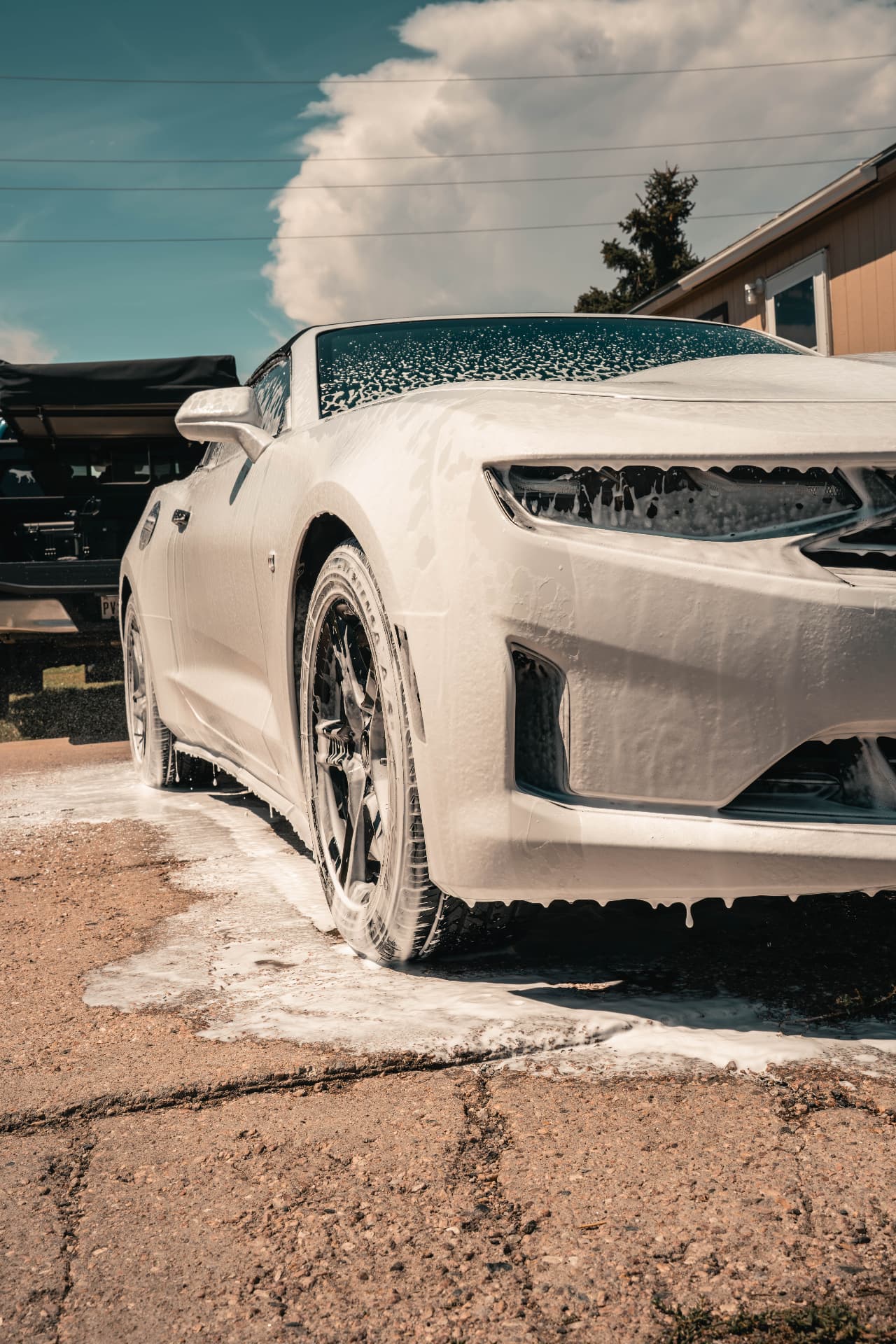 White Camaro convertible covered in thick snow foam during a mobile wash